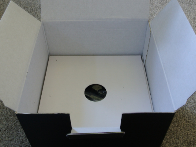 The second layer in the box showing a cardboard insert with a round hole in the middle