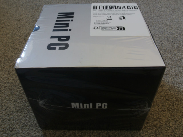 The T8 box in protective transparent shrink wrap. The top of the box is sliver-grey and says &ldquo;Mini PC&rdquo;, with a similar logo on the darker anterior side of the box